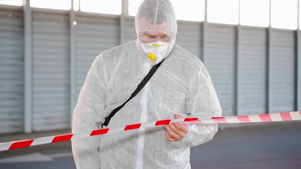 Hombre, trabajador parado línea fronteriza señal de advertencia desinfecta, pulveriza productos químicos en la superficie contra el coronavirus. Medidas sanitarias en lugar público durante la cuarentena — Vídeo de stock