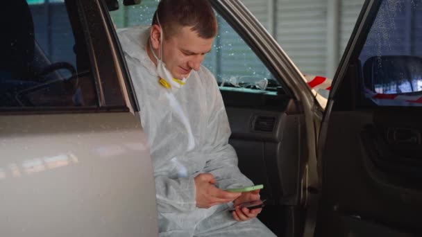 男性医療従事者医師服を着た白い保護全体座って車の休憩を使用してスマートフォン — ストック動画