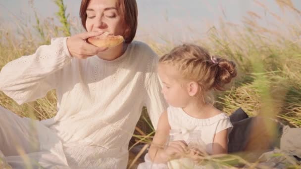 Anya a gyerekekkel a természetben ebédel kenyérrel és tejjel. Boldog tanyasi család piknikező búza mező — Stock videók