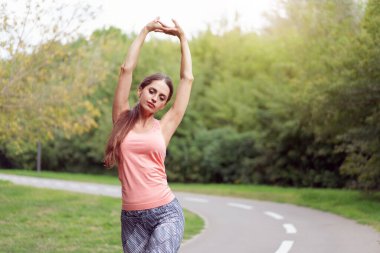 Yaz parkında koşmadan önce kollarını esneten kadın koşucu orta yaşlı atletik kadın vücudu ısıtıyor, beyaz kadın ısınıyor, koşuyor, koşuyor şehir parkında koşuyor.