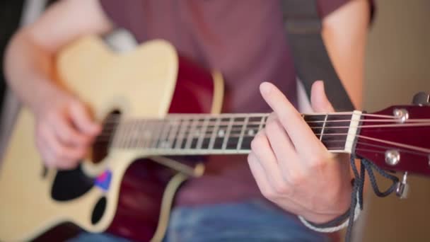 총을 가까이 놓고 앉아서 어쿠스틱 기타를 치고 있는 잘생긴 청년 — 비디오