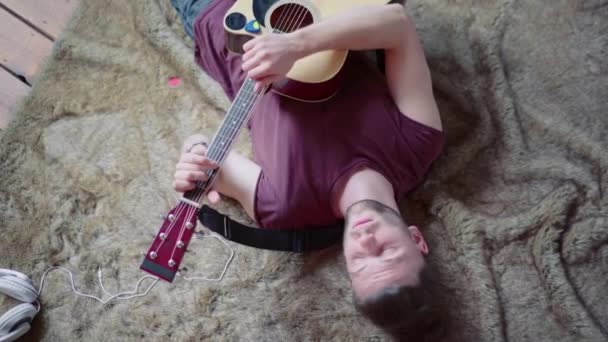 Muž s akustickou kytarou zpívající a hrající na kytaru ve lživé poloze. Horní pohled. Útěk z nudy. — Stock video
