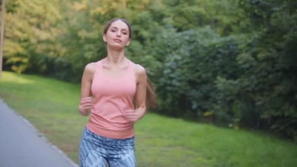 Спортивная женщина бегает беговая дорожка в парке летний день Кавказская женщина бег трусцой одет спортивная одежда Средняя съемка — стоковое видео