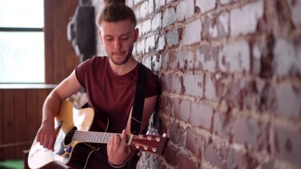 Чоловік з акустичною гітарою, що спирається на цегляну стіну, грає пісні співу, насолоджується життям Середня стрілянина — стокове відео