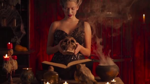 Halloween häxa med kittel och magi bok. Vacker ung kvinna trollar, gör häxeri — Stockvideo