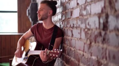 Akustik gitarı olan, tuğla duvara yaslanan, müzik çalan, hayattan zevk alan, orta boy, mesaj için boş alan olan bir adam.