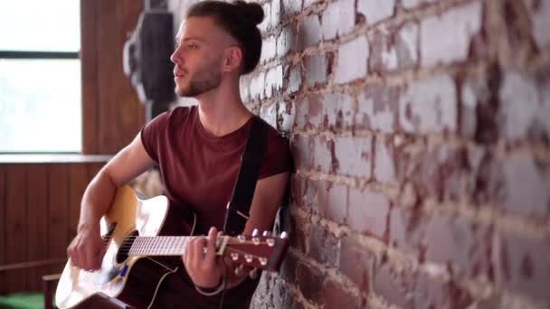 Człowiek z gitarą akustyczną opierając się o cegły ściany odtwarzanie muzyki śpiew piosenki cieszyć się życiem Medium shoot Wolne miejsce na tekst — Wideo stockowe
