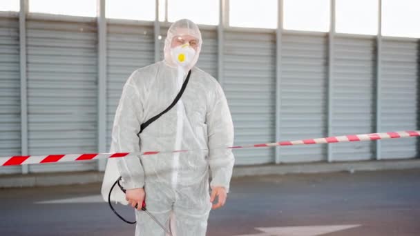Man, worker standing border line warning sign disinfects, sprays chemicals on surface against coronavirus. Sanitary measures in public place during quarantine — Stock Video