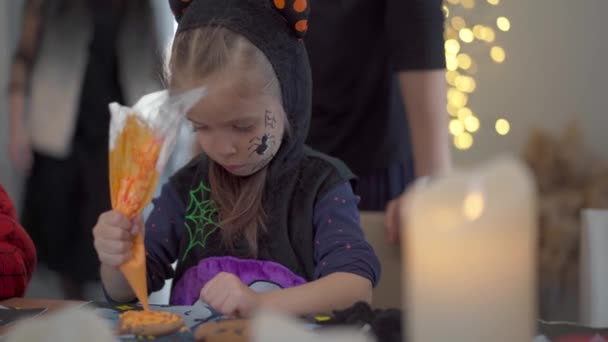 Klein meisje versieren glazuur handgemaakte Halloween koekjes gekleed Halloween carnaval kostuum met hoorns — Stockvideo