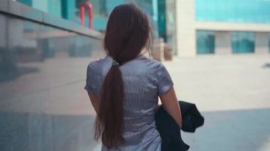 İş kadını, şehir sokaklarında yaz günü yürüyen beyaz kadın iş adamına gülümsemektense kamerayı takip ederek yürür.