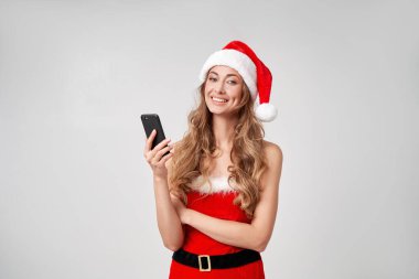 Noel Baba Beyaz Şapkalı Kadın stüdyosunun arka planında elinde akıllı telefon güzel beyaz kadın kıvırcık saçlı portresi var. Mutlu insan pozitif duygu. Fotokopi alanı ile tatil kavramı. Gülümseyen diş. 