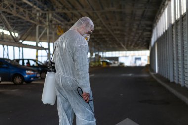 Koruyucu giysi giyen işçiler dezenfekte ekipmanları halka açık bir yerde park ediyorlar. Genel olarak dezenfektan güvenliği ve solunum maskesi Covid salgını önleyici tedbirler