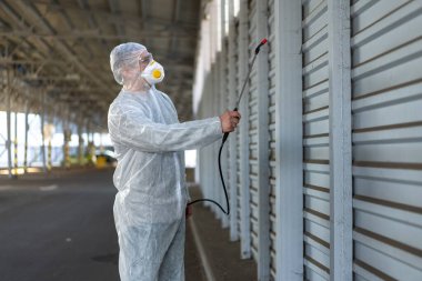 Koruyucu giysi giyen işçiler dezenfekte ekipmanları halka açık bir yerde park ediyorlar. Genel olarak dezenfektan güvenliği ve solunum maskesi Covid salgını önleyici tedbirler