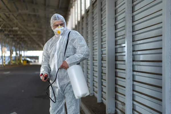 Worker wearing protective suit disinfection gear disinfect surface public place parking. Side view of disinfector safety overall and respiratory mask Covid pandemic disinfection preventive measures