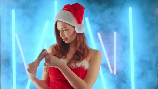 Weihnachtsverkaufs-Konzept Frau im Weihnachtsmannkostüm S Weihnachtsmannmütze mit Geld in der Hand im Stehen beleuchtet Neonhintergrund — Stockvideo