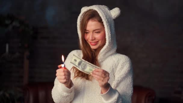 A fiatal nő dollárokat éget. Gyönyörű kaukázusi nő, fehér kapucnis pulóver fülekkel pénzt tart a kezében, és felgyújtja az öngyújtójukat. — Stock videók