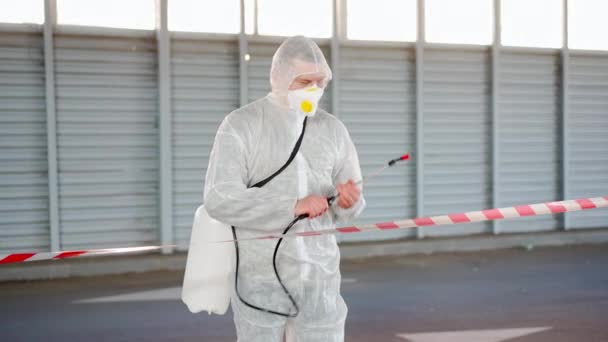 Muž, pracovník stojící na pohraniční čáře varovné znamení dezinfikuje, stříká chemikálie na povrch proti koronaviru. Sanitární opatření na veřejném místě během karantény — Stock video