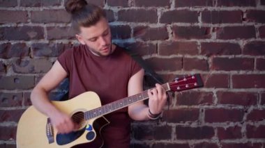 Akustik gitarlı bir adam tuğladan duvara yaslanmış müzik çalıyor ve hayattan zevk alıyor.