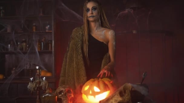 Halloween concept. Black witch holding Halloween pumpkin with carved smily face in hand standing dark room — Stock Video