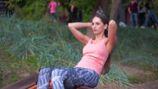 Atletisk kvinna gör magövningar på bänk träningsmaskin utomhus gym i park vacker stark professionell atletisk kvinna träning utanför — Stockvideo