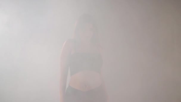 Artistic young woman dancing in backlit fog smoke indoors. Confident graceful Caucasian female dancer rehearsing modern performance with ballet movements — Stock video