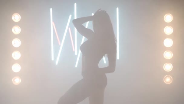Mujer joven artística bailando en humo de niebla retroiluminada en interiores. Bailarina femenina caucásica confiada ensayando actuación moderna con movimientos de ballet — Vídeo de stock
