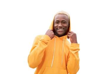 Genç siyah adam mutlu, pozitif ve başarılı hissediyor, kapüşonu tutuyor, başarıları beyaz arka planda izole edilmiş. Afrika kökenli erkek, sarı saçlı, sarı kapüşonlu.