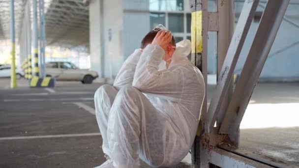 Працівник охорони здоров'я у білому кованому захисному комбінезоні. Втомлений чоловік кавказький лікар захоплює голову в депресії під час пандемії коронавірусу — стокове відео