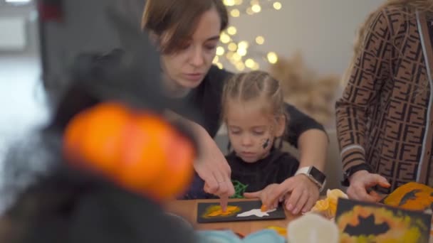 Kislány öltözött Halloween karnevál jelmez anyja ül az asztalon rajz kézzel készített Halloween dekoráció party — Stock videók