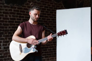 Akustik gitarlı bir adam beyaz tahta müzik okulu konseptinin yanında duruyor. Beyaz tenli erkek gitarist kapalı mekanda yazı tahtası ile.