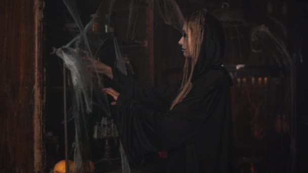 Penyihir Halloween mengambil ramuan dari rak dengan jaring laba-laba, lilin di latar belakang, sihir di mana-mana — Stok Video
