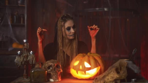 Concepto de Halloween. Bruja negra calabaza de Halloween con cara sonriente tallada sentada en la mesa habitación oscura mostrando sangre en las manos — Vídeos de Stock