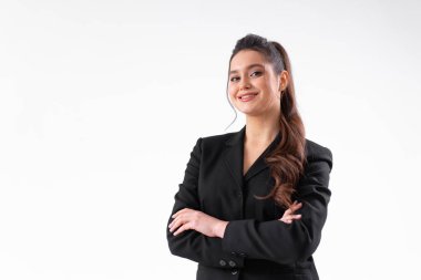 Siyah ceketli genç iş kadını kolları beyaz arka planda izole bir şekilde stüdyoda duruyor. Beyaz kadın iş adamı kameraya bakıyor ve gülümsüyor. Orta karar atış.