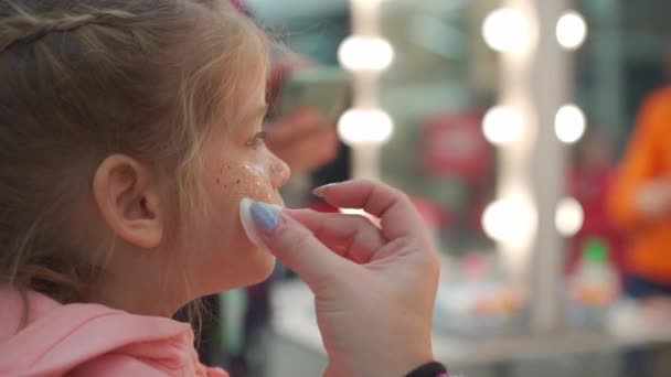 Niña en un salón de belleza. Maquillaje artista aplicar maquillaje para el niño mientras mamá filma el proceso en el teléfono inteligente — Vídeos de Stock