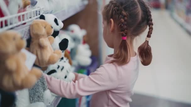 Little Child pede a sua mãe para comprar um brinquedo macio de tigre branco na loja de departamento infantil. Crianças do sexo feminino caucasianas escolhem brinquedo animal fofo no supermercado — Vídeo de Stock