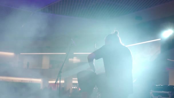 Чоловік грає на етнічних барабанах, стоячи на сцені в димі і прожекторах — стокове відео