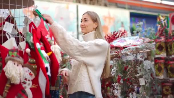 Різдвяні магазини, європейська жінка, одягнена в білий светр, вибирають роги оленів у супермаркеті, надягають на голову і посміхаються, дивлячись на камеру. Костюм самки - білоруки 30 років. — стокове відео