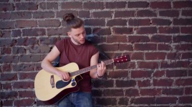 Akustik gitarlı bir adam tuğladan duvara yaslanır müzik besteler şarkı söyler hayatın tadını çıkar orta yaş çekimi