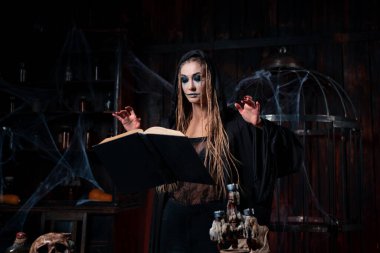 Cadılar Bayramı konsepti Kara başlıklı cadı karanlık zindan odasında büyü yapmak için sihirli kitap kullanıyor. Kadın büyücü büyücü Gotik iç mimari Kafes, örümcek ağı