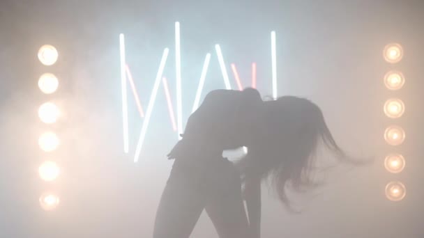 Mujer joven artística bailando en humo de niebla retroiluminada en interiores. Bailarina femenina caucásica confiada ensayando actuación moderna con movimientos de ballet — Vídeos de Stock