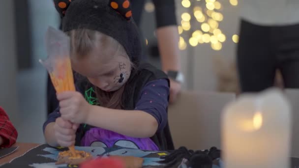 Kleines Mädchen dekoriert Zuckerguss handgemachte Halloween-Plätzchen gekleidet Halloween Karneval Kostüm mit Hörnern — Stockvideo