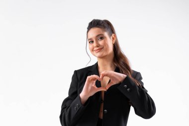 Genç iş kadını, beyaz arka planda izole edilmiş siyah ceketli kalp hareketi sergiliyor. Beyaz kadın iş adamı kameraya bakıyor ve gülümsüyor. Orta karar atış.