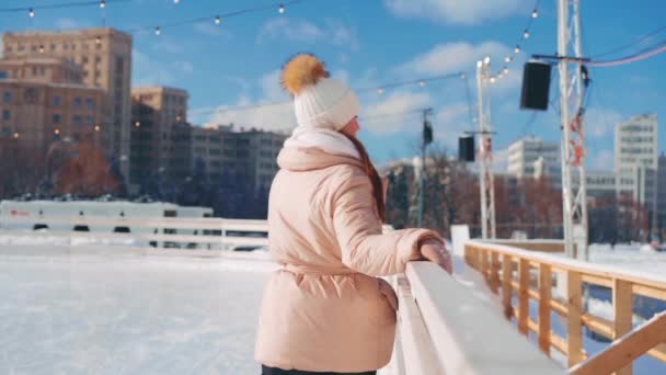 Νεαρή χαμογελαστή γυναίκα παγοδρομία έξω στο παγοδρόμιο κεντρική πλατεία της πόλης στις διακοπές των Χριστουγέννων, ενεργό χειμερινό ελεύθερο χρόνο σε ζεστή ηλιόλουστη μέρα. Εφέ χειρός. Ερασιτέχνης καυκάσιος γυναικάς παγοδρόμος — Αρχείο Βίντεο