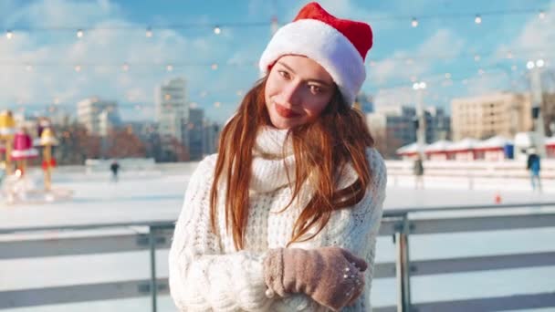 Gülümseyen genç kadın Noel Baba, buz pateni pistinde beyaz kazak giyerek buz pateni yapıyor. Noel tatili, aktif kış tatili el bilgisayarı etkisi. Amatör beyaz kadın buz patencisi. — Stok video