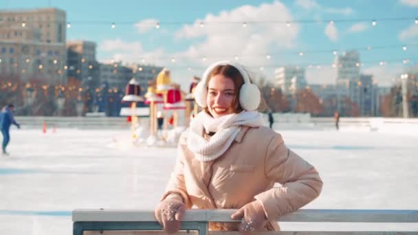 Joven mujer sonriente patinaje sobre hielo al aire libre en pista de hielo plaza de la ciudad central vacaciones de Navidad, gesto a mano invitar a amigos en pista de patinaje sobre hielo, ocio activo invierno en un día cálido y soleado. — Vídeos de Stock
