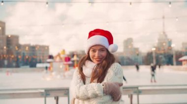 Gülümseyen genç kadın Noel Baba, buz pateni pistinde beyaz kazak giyerek buz pateni yapıyor. Noel tatili, aktif kış tatili el bilgisayarı etkisi. Amatör beyaz kadın buz patencisi. 
