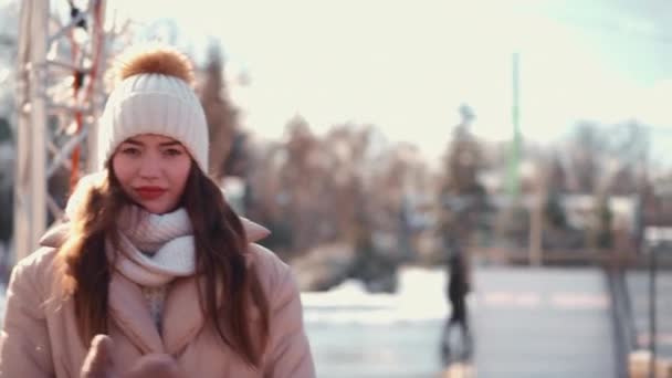 Junge Frau in Winterjacke mit weißer Strickmütze und Schal steht draußen auf der Winterstadtstraße — Stockvideo