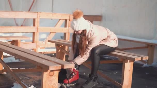 Mujer joven preparando patinaje. Mujer caucásica atando cordones de patines de hielo sentados en el banco al aire libre. Atando patines rojos. Vacaciones de Navidad ocio activo en la naturaleza. — Vídeos de Stock