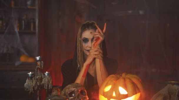 Halloween-Konzept. Schwarze Hexe Halloween-Kürbis mit geschnitztem smily Gesicht sitzt auf dem Tisch dunklen Raum zeigt Blut an den Händen — Stockvideo