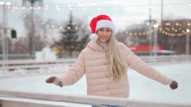 Kış zamanı. Noel tatili, Santa Şapkalı bir kadın şehir meydanında buz pateni pistinde kayıyor. Kış mevsimi. Beyaz, yetişkin, amatör buz patencisi kadın. 